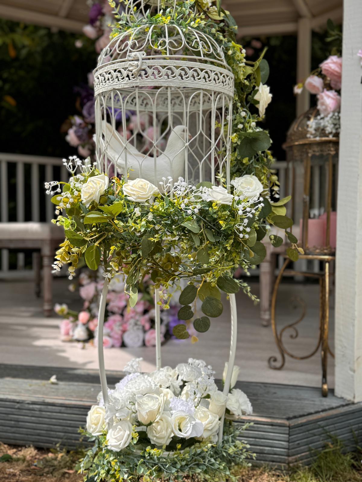 A white dove in an ornate birdcage adorned with roses and greenery