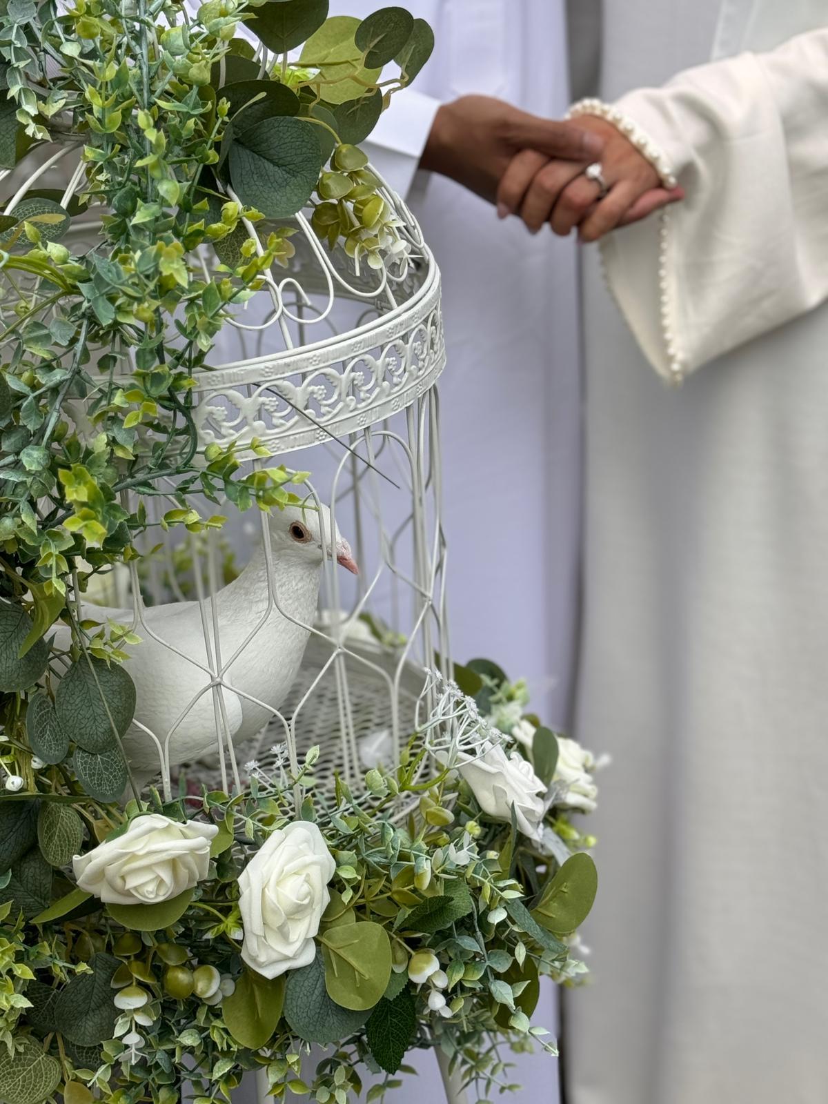 A white dove in a floral birdcage with a couple holding hands softly behind