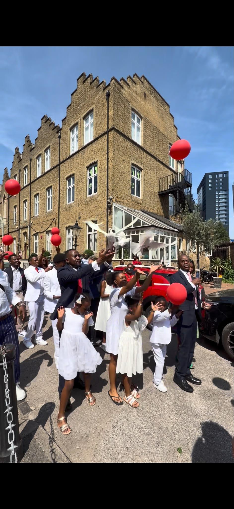 Guests and children watching white doves rise among red balloons outdoors