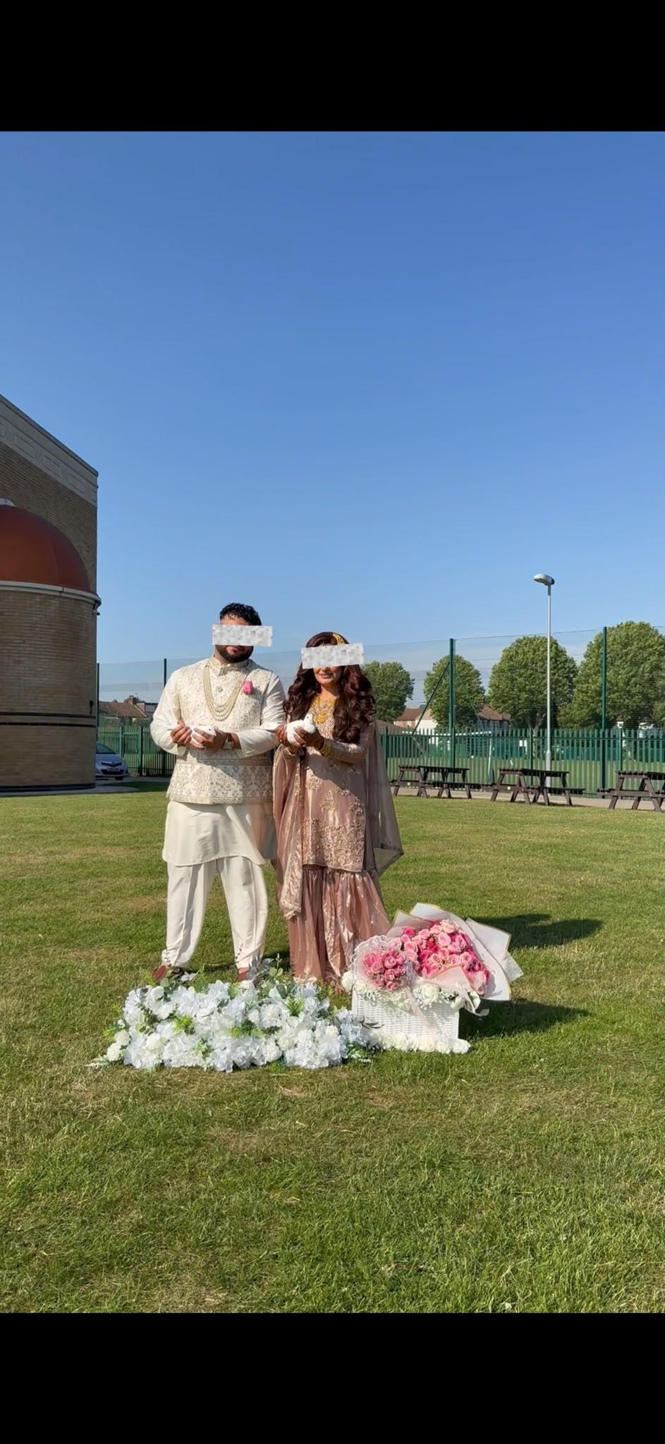 A couple in traditional attire holding white doves on a sunlit lawn with floral arrangements