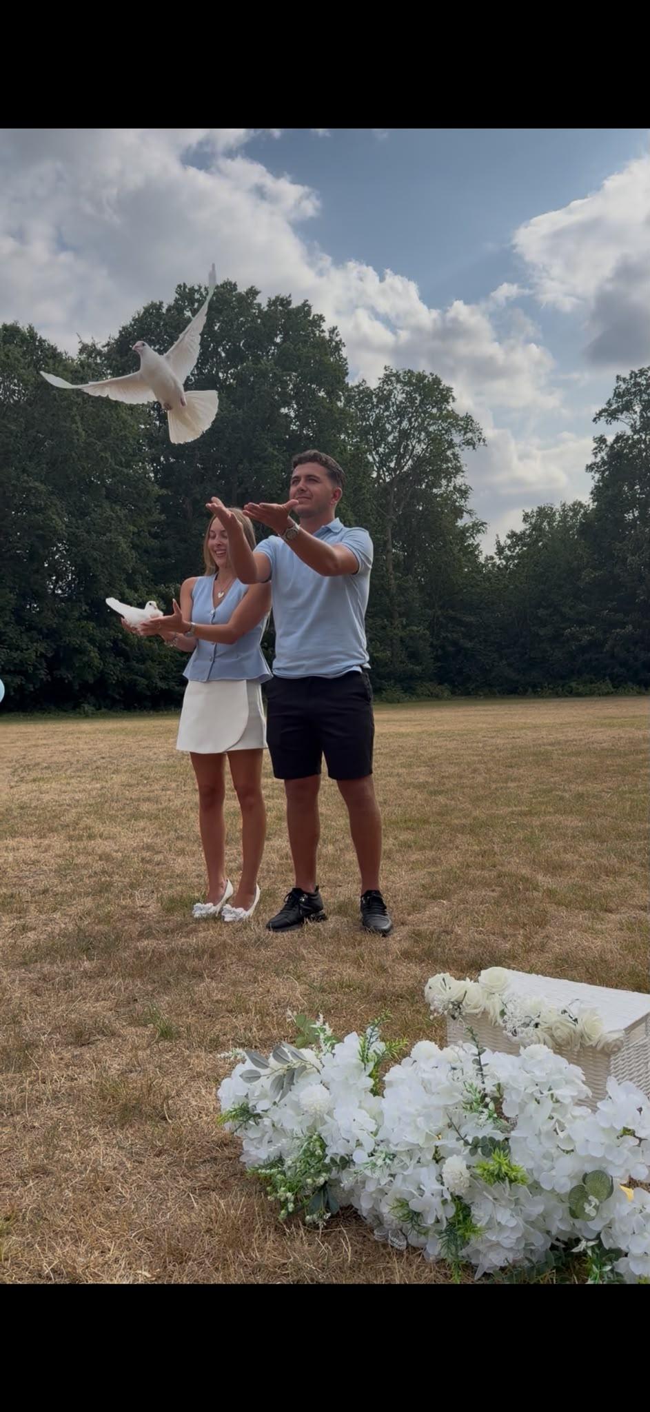 A couple releasing white doves into a bright sky above a grassy field
