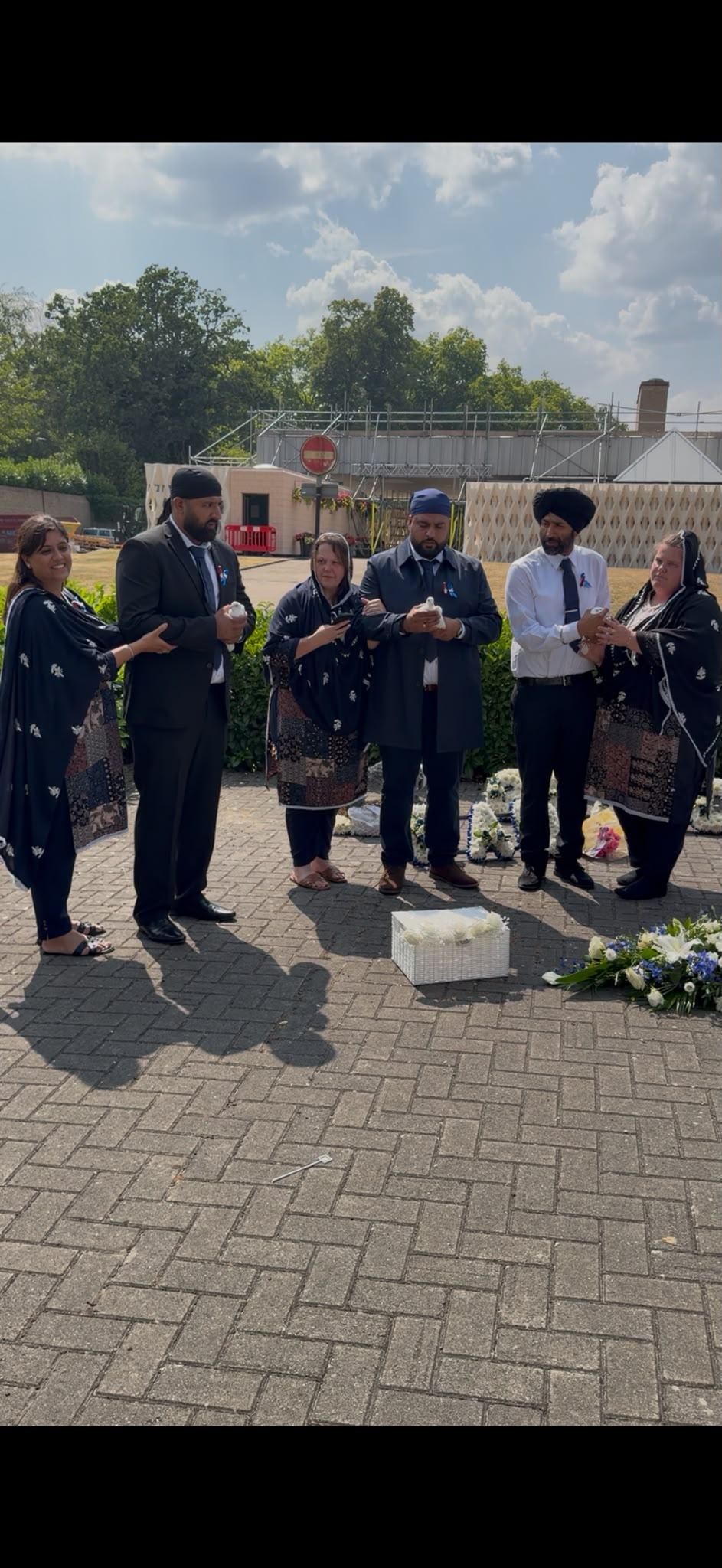 A family gathered outdoors holding white doves beside floral tributes